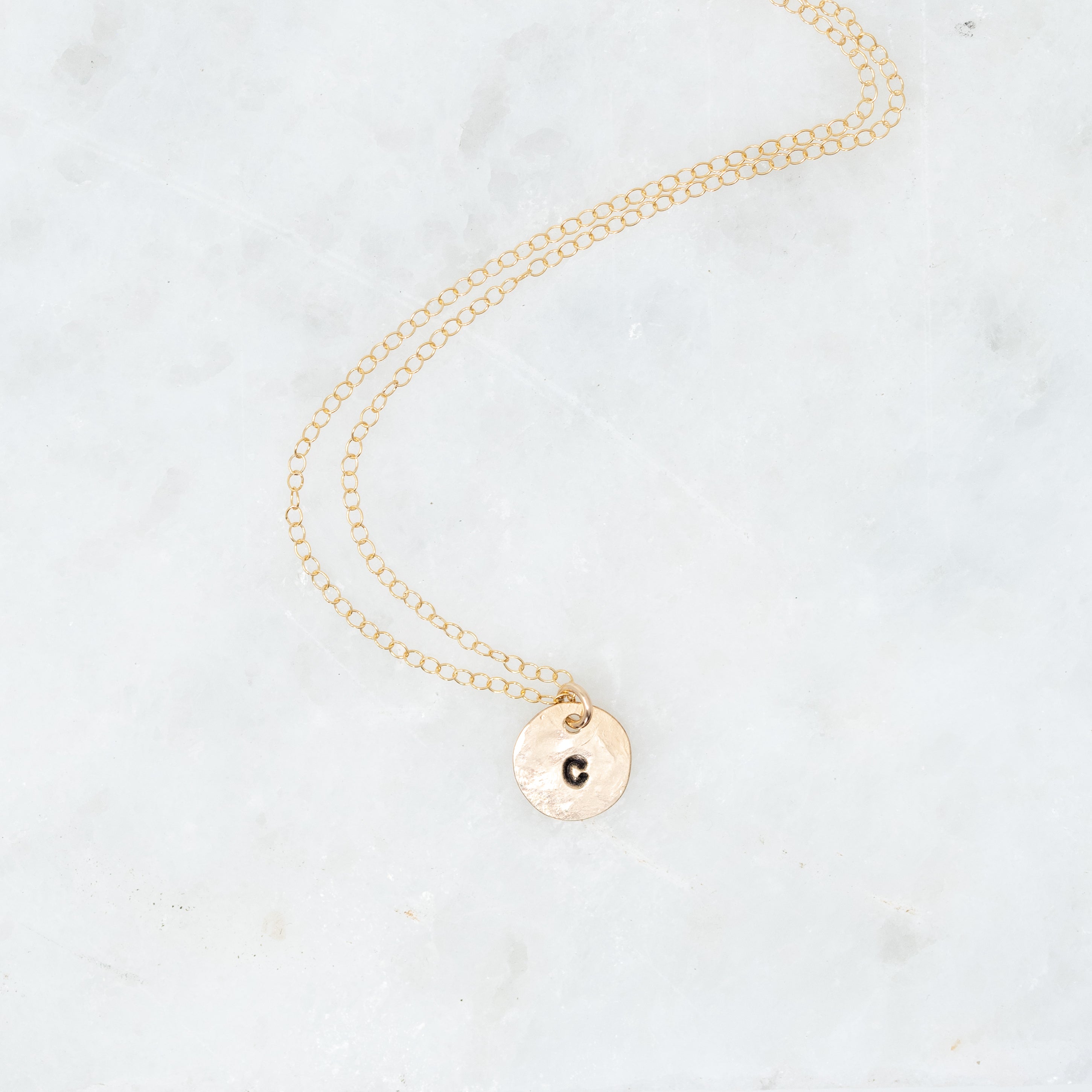 Tiny gold filled circle with initials stamped onto it. On a gold chain. 