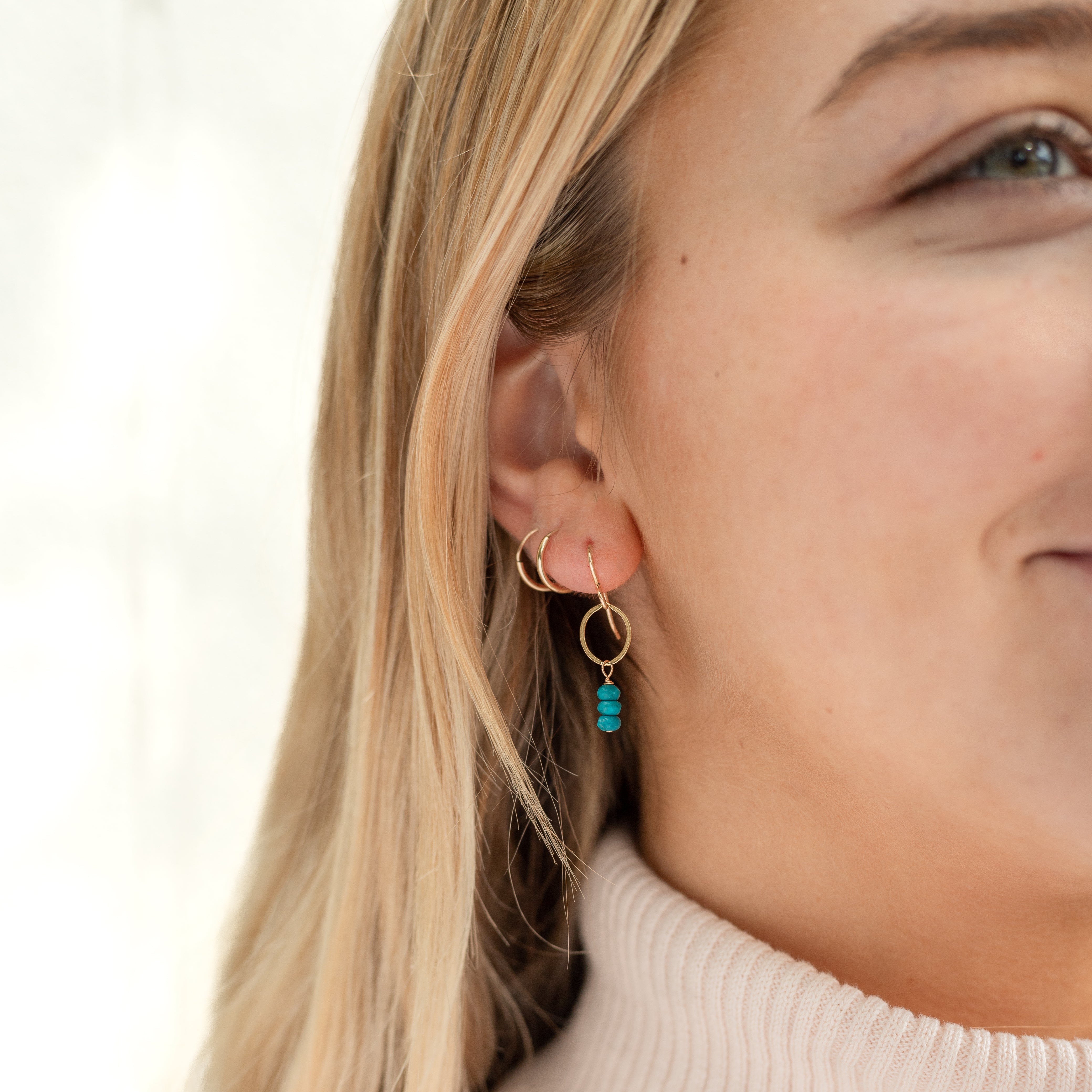 Gold filled tiny hoop with turquoise beads hanging from the bottom of the loop. Shown in a woman's ear. 