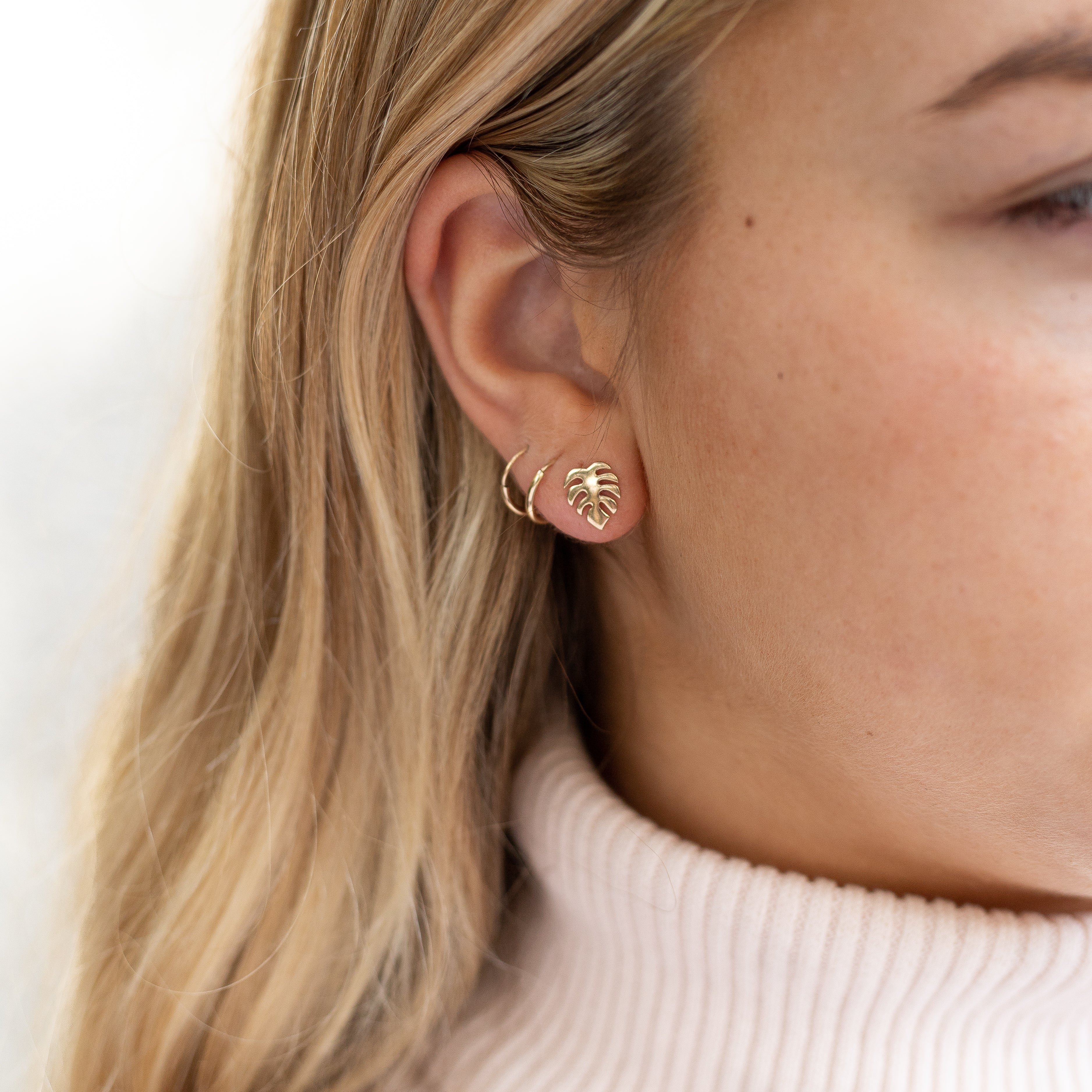 Tiny gold filled monstera leaf studs shown in a woman's ear. 