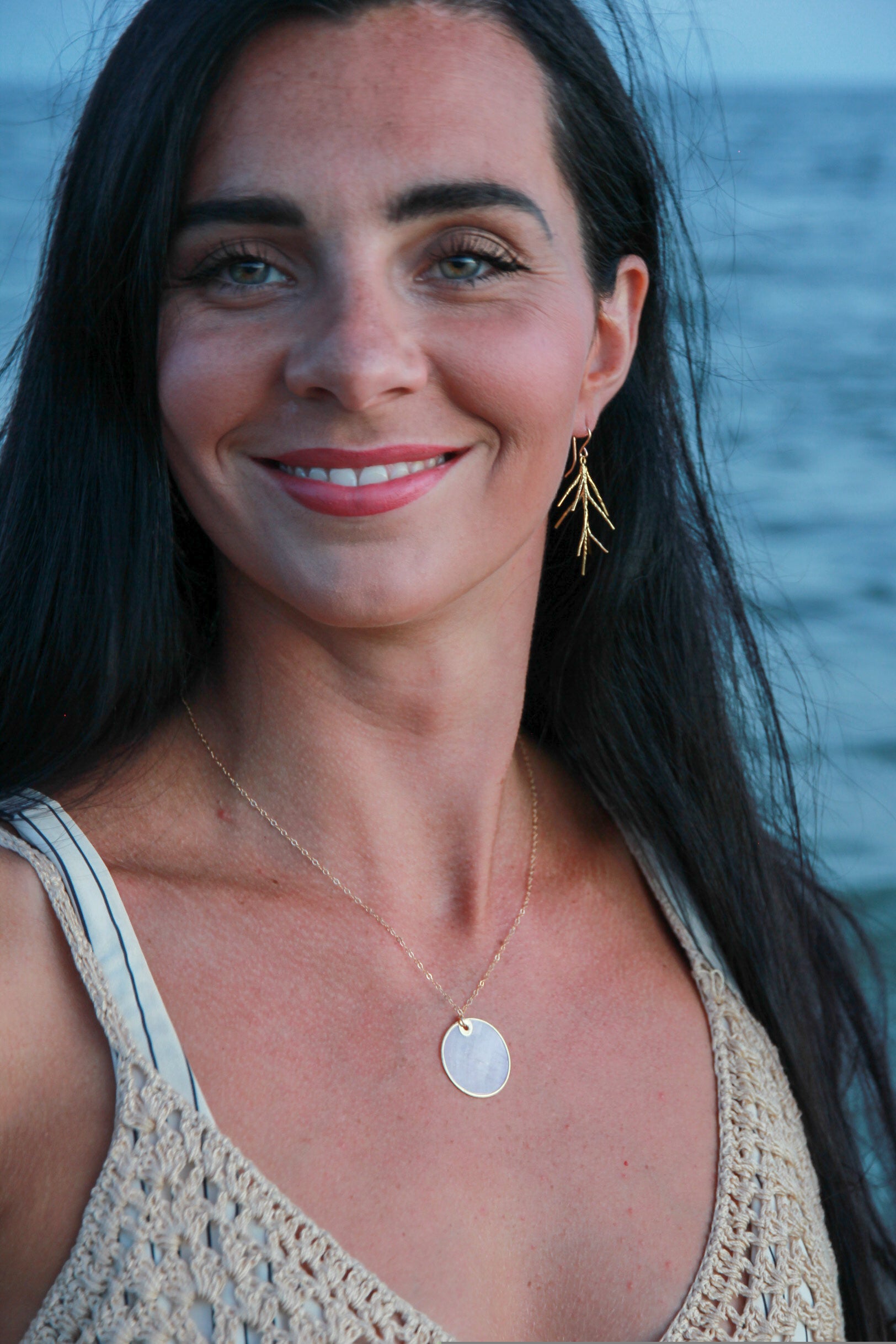 Brass twig earrings shown in a woman's ear on the beach. 