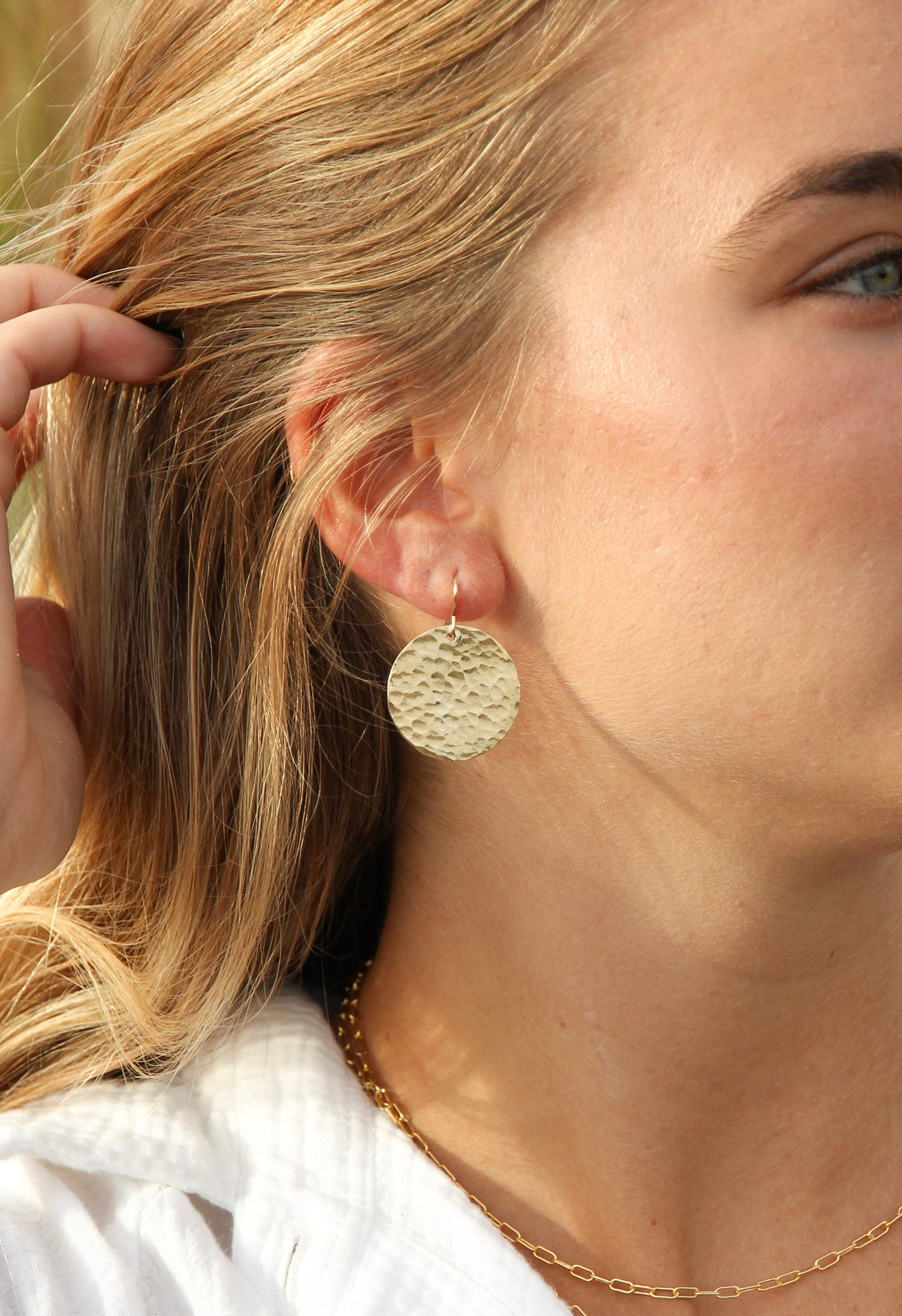 Gold filled hammered disk earrings shown in a woman's ears.