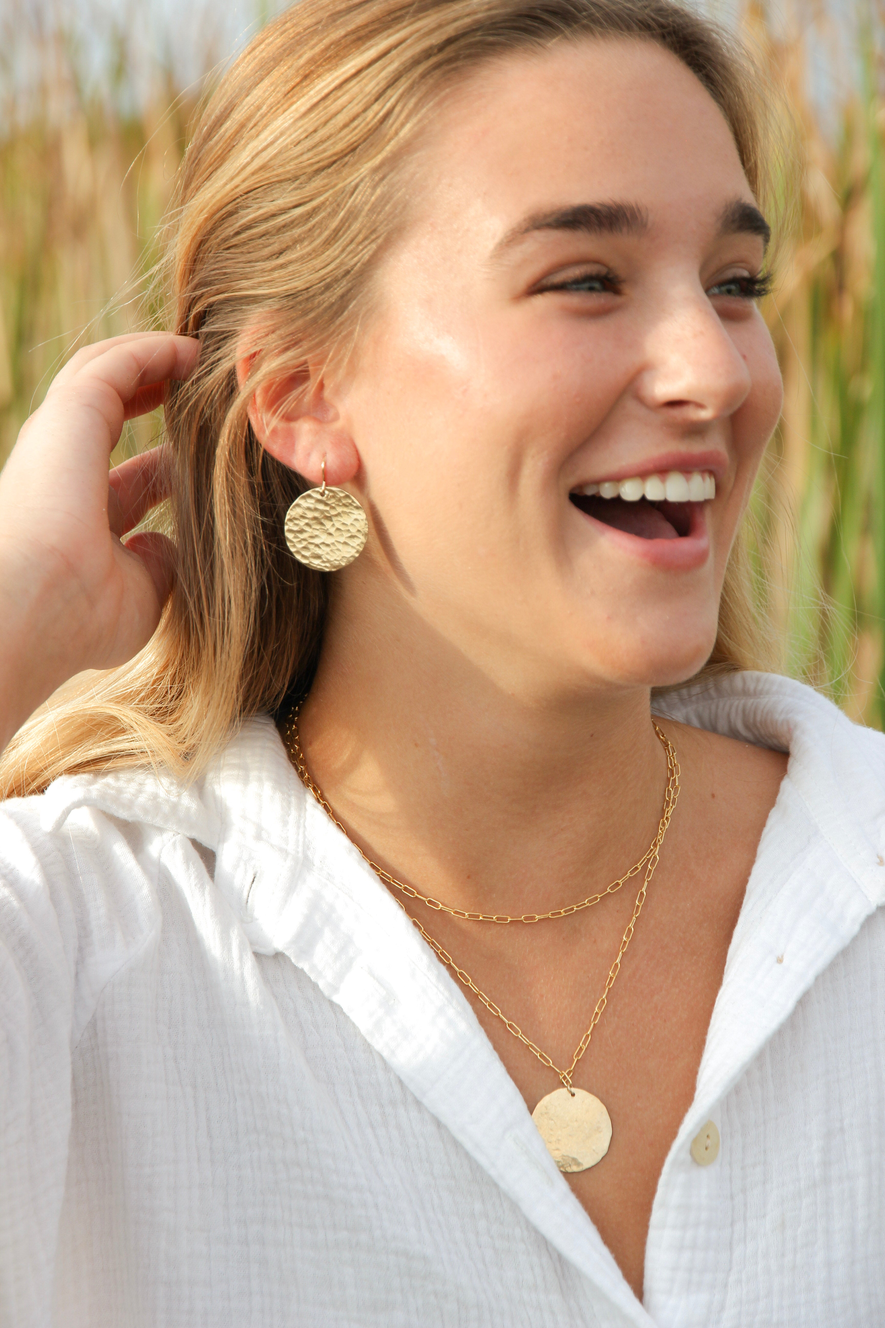 Large hammered gold disk earrings shown in a woman's ears.