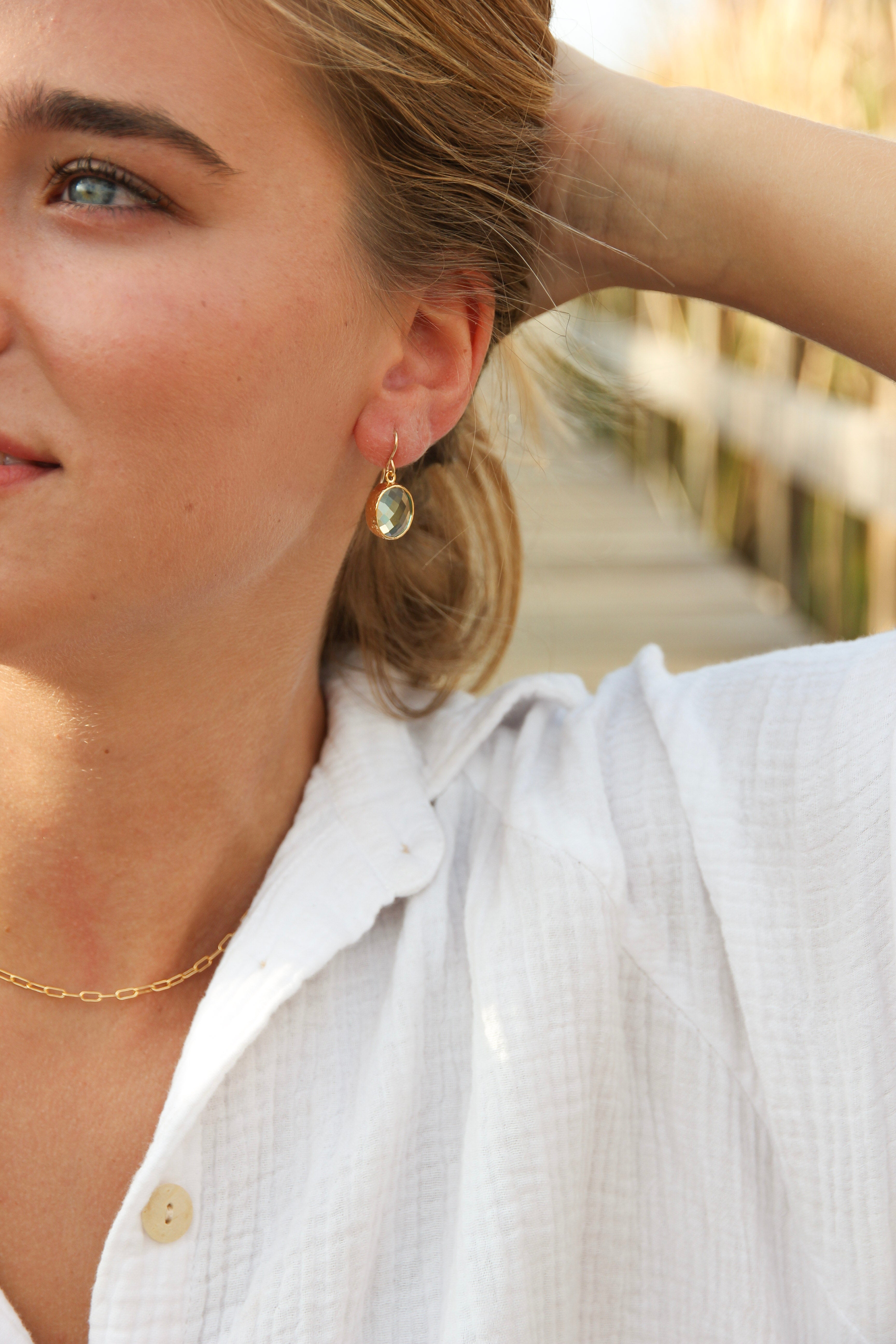 Blue topaz earrings with gold plated rim shown in a woman’s ear 