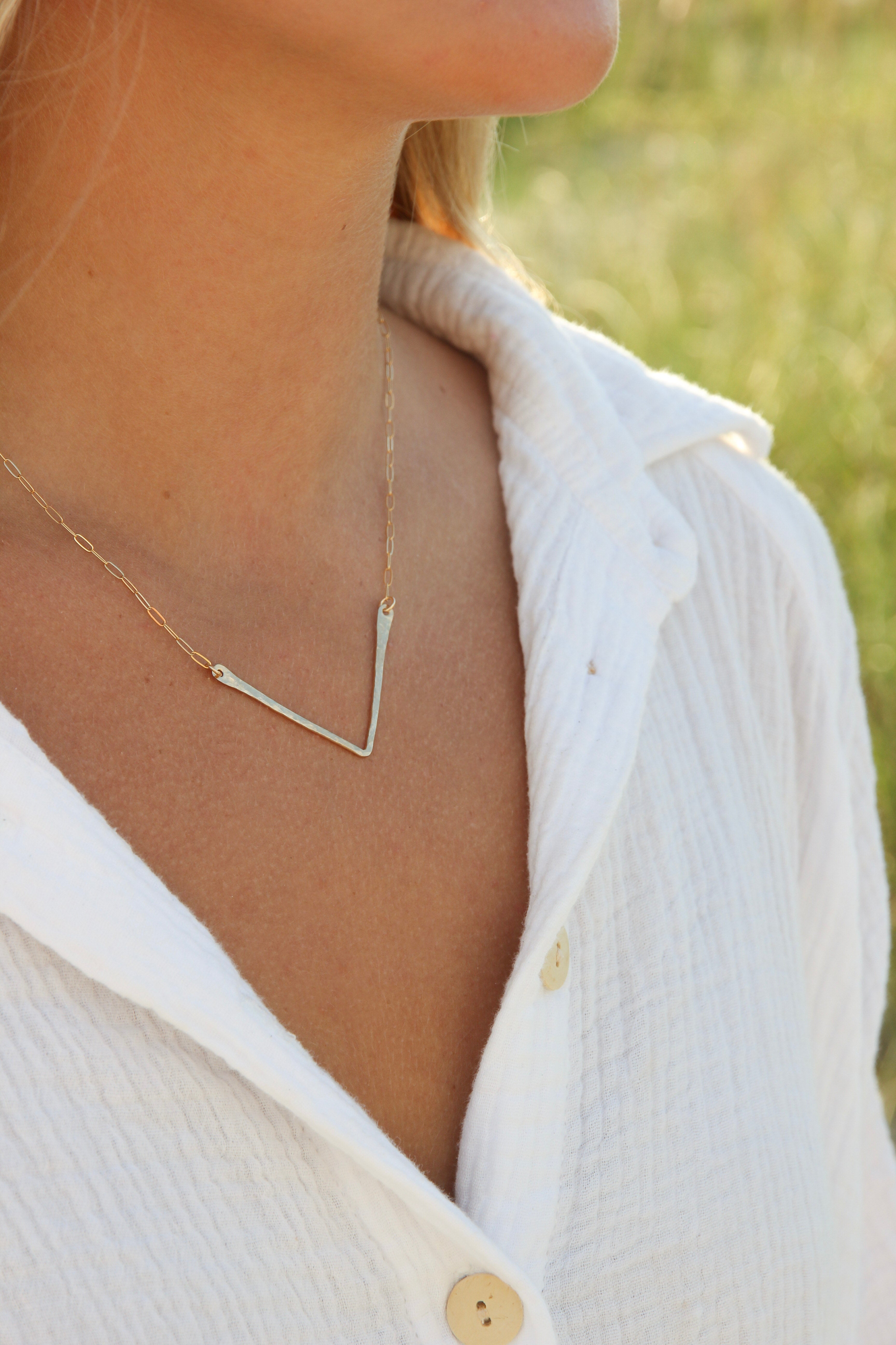 Hand forged V shaped gold bar attached to a gold chain shown on a woman's neck. 