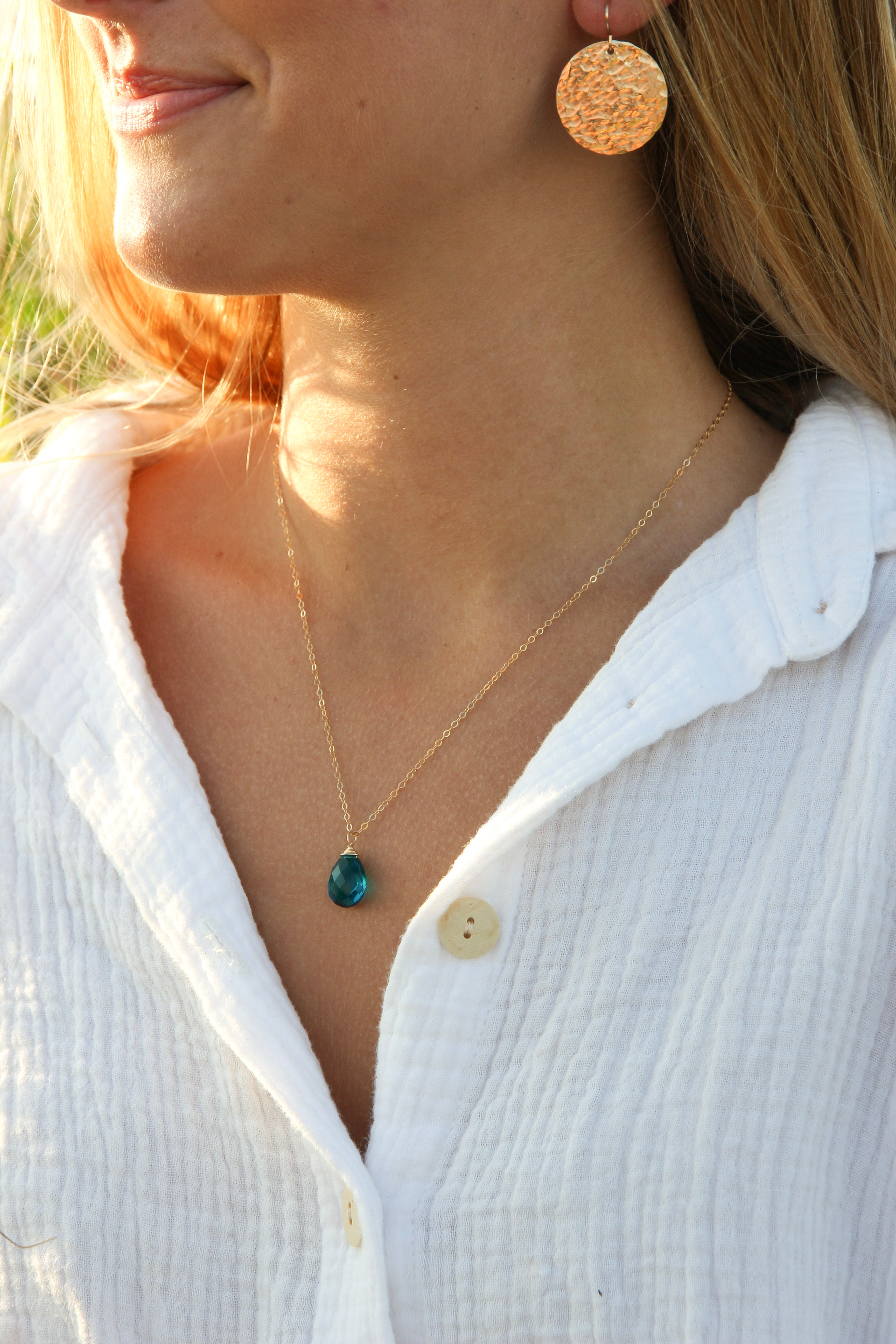 Crystal teal teardrop stone wire wrapped with gold wire on a simple gold chain.  Shown on a woman's neck. 