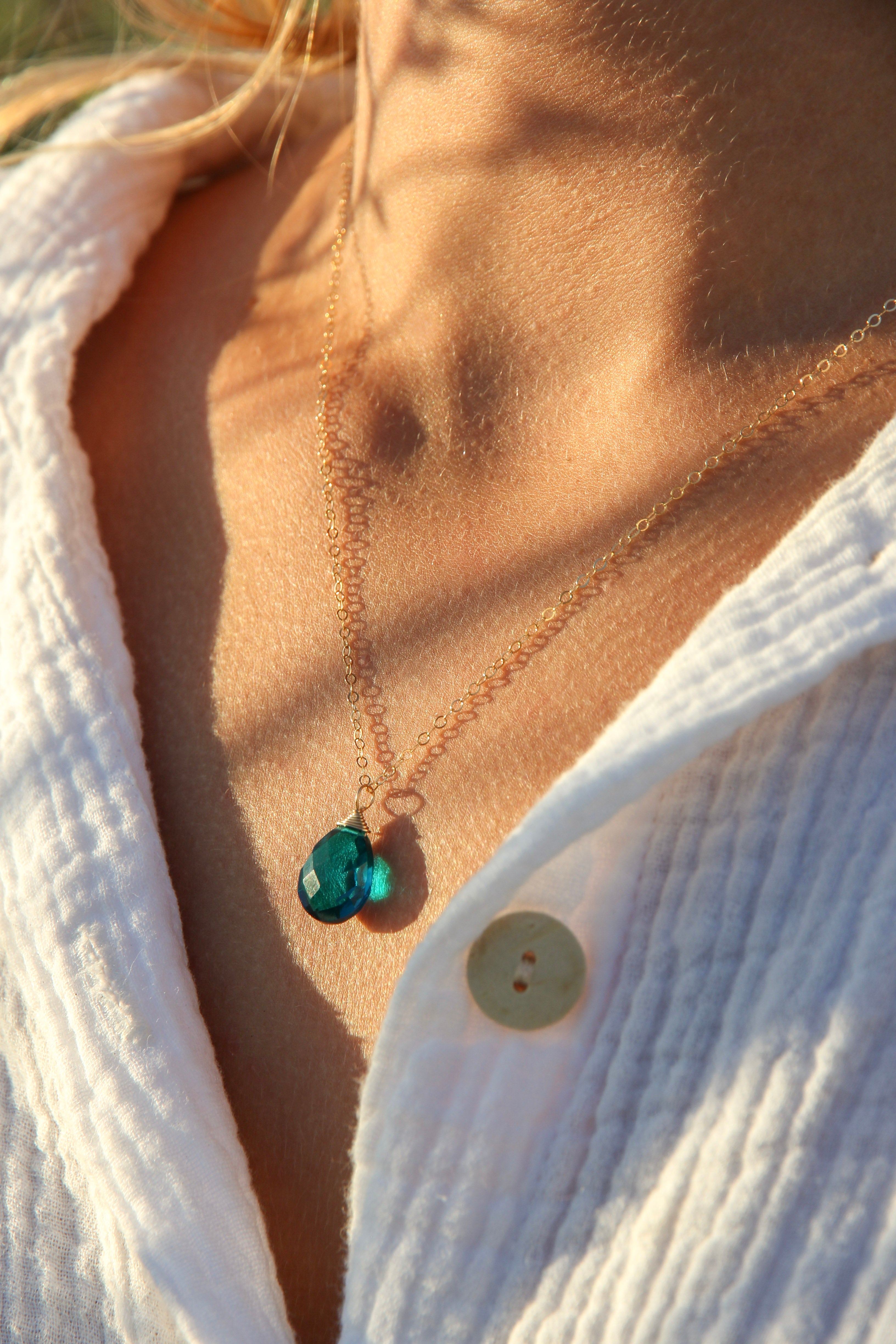 Crystal teal teardrop stone wire wrapped with gold wire on a simple gold chain.  Shown on a woman's neck. 