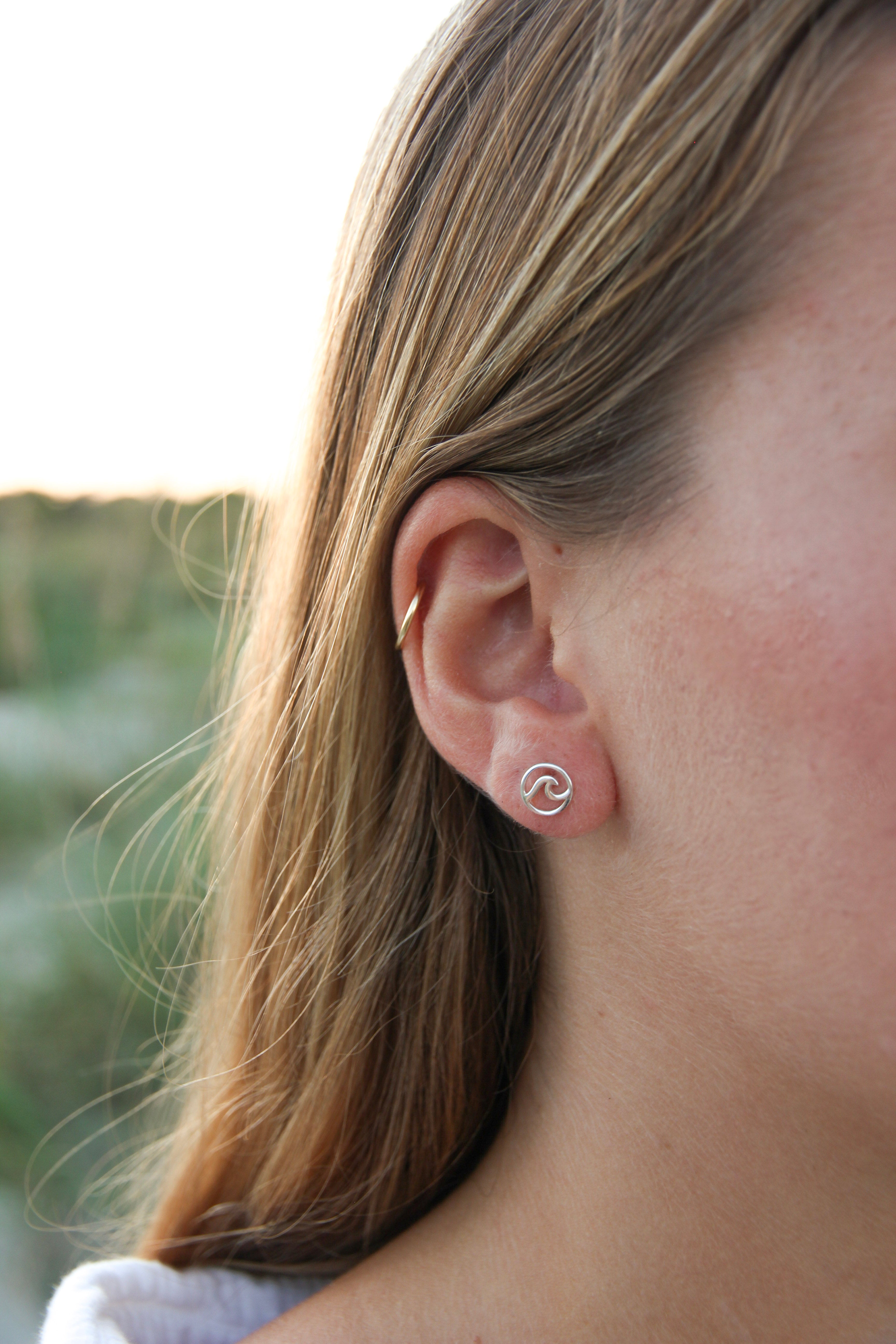 small silver studs with a wave in the middle shown on a woman's ear. 