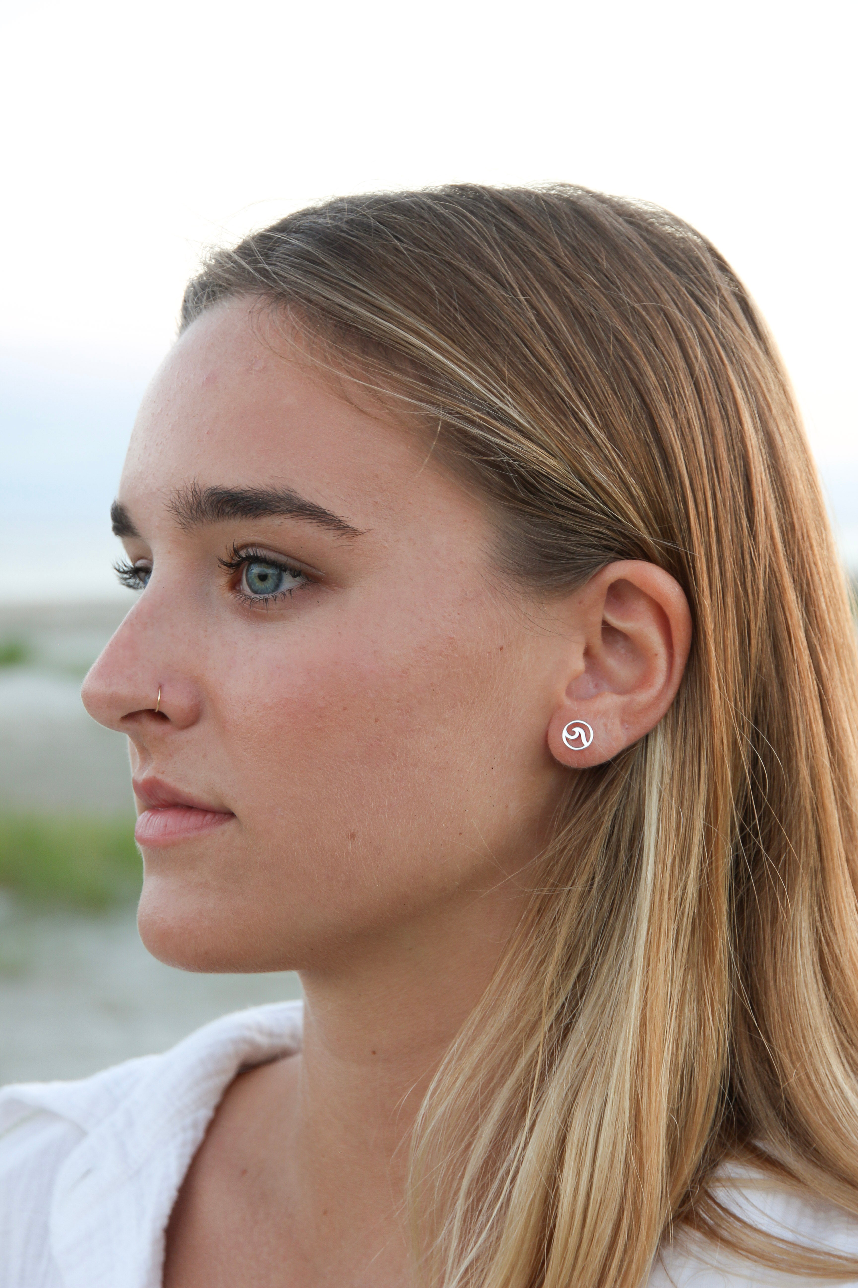 small silver studs with a wave in the middle shown in a woman's ear.