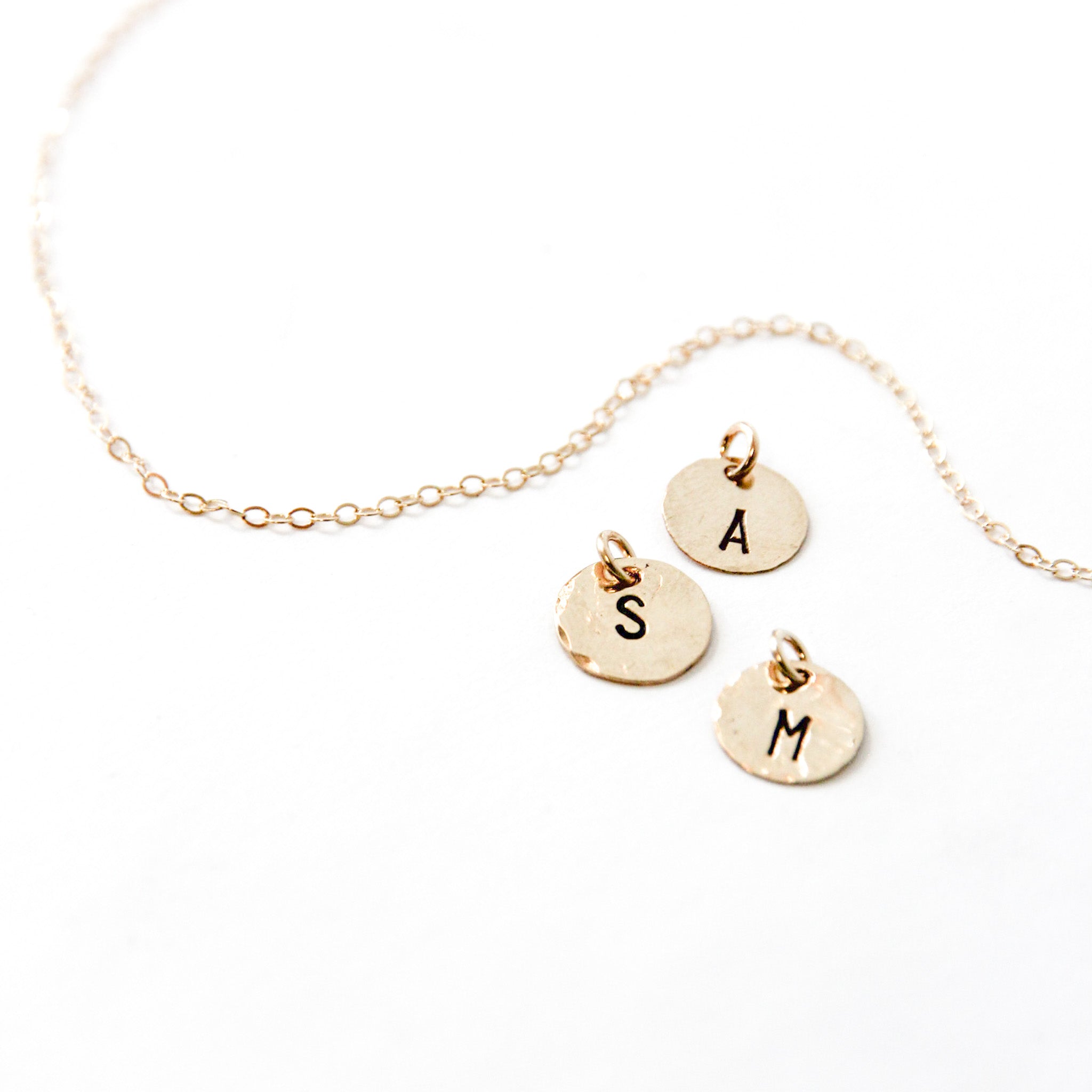 Three small gold circle charms about one third of an inch next to gold chain with the letters  A, S and M on them