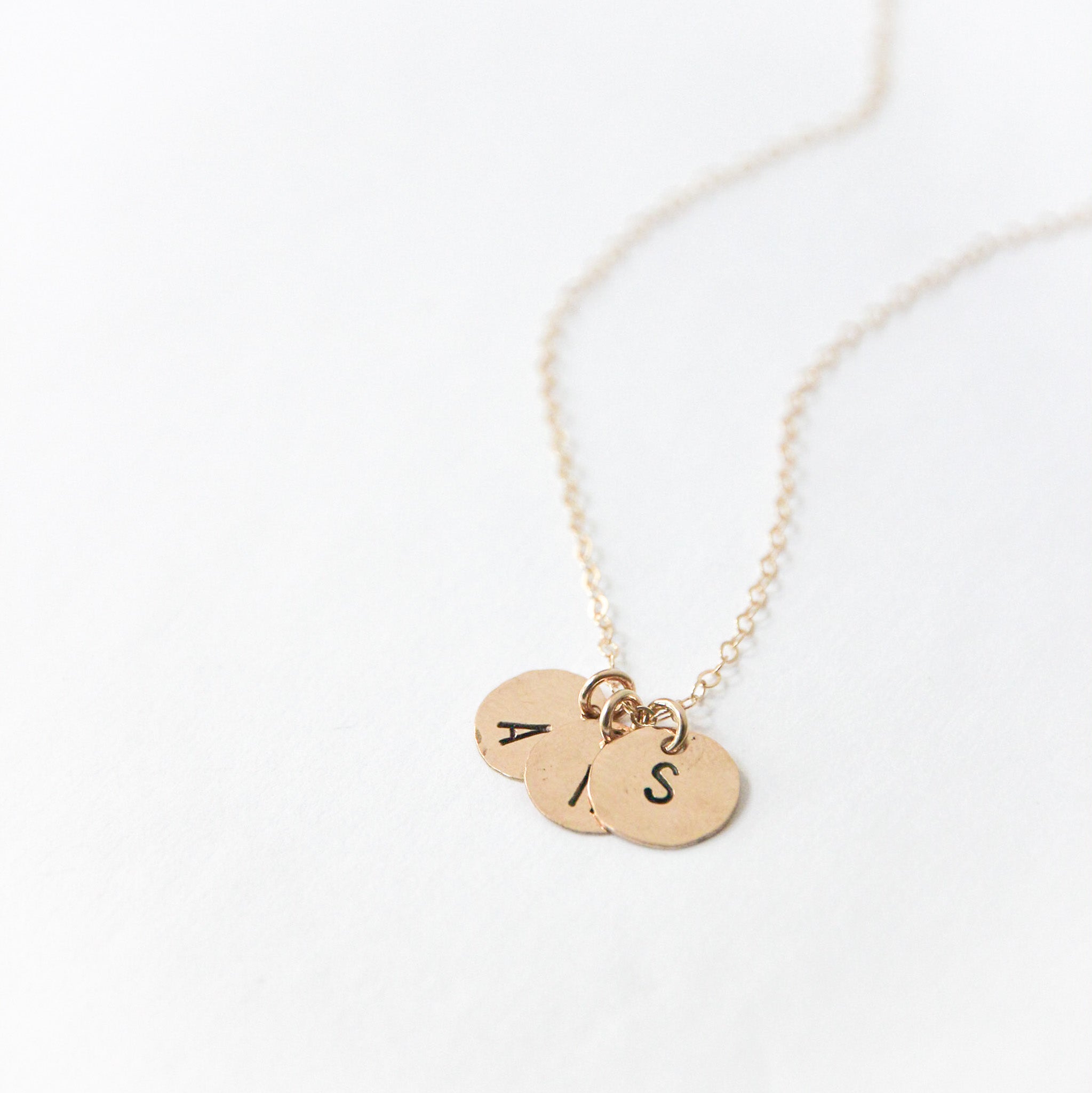 Three small gold circle charms about one third of an inch attached to the chain with stamped letters on them
