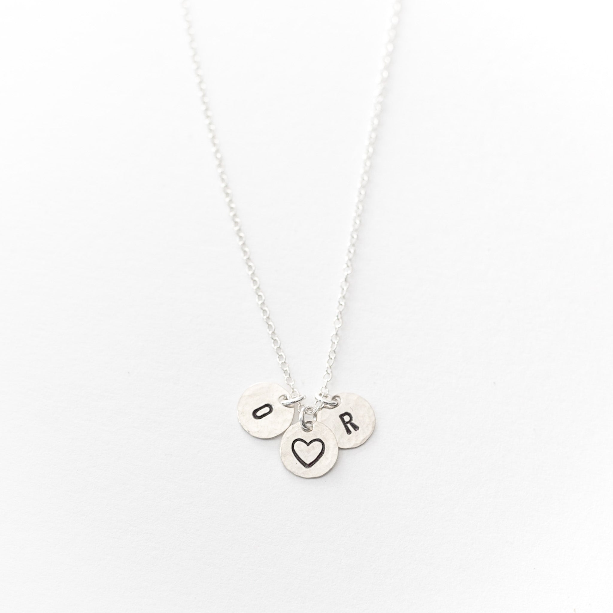 Three silver charms about one third of an inch attached to a silver chain. There’s a O, heart, and R stamped on them 