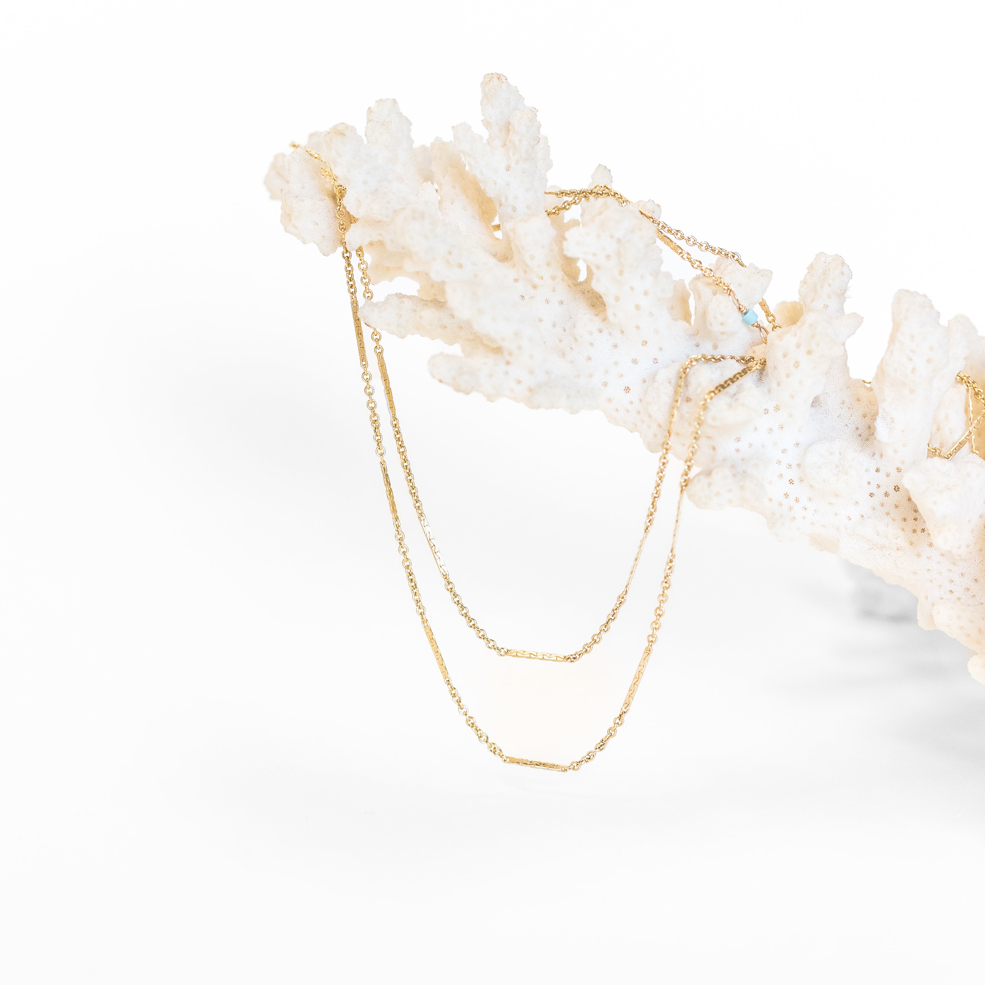 Dainty gold thin necklace that wraps around your neck two times. Displayed on a piece of coral. 