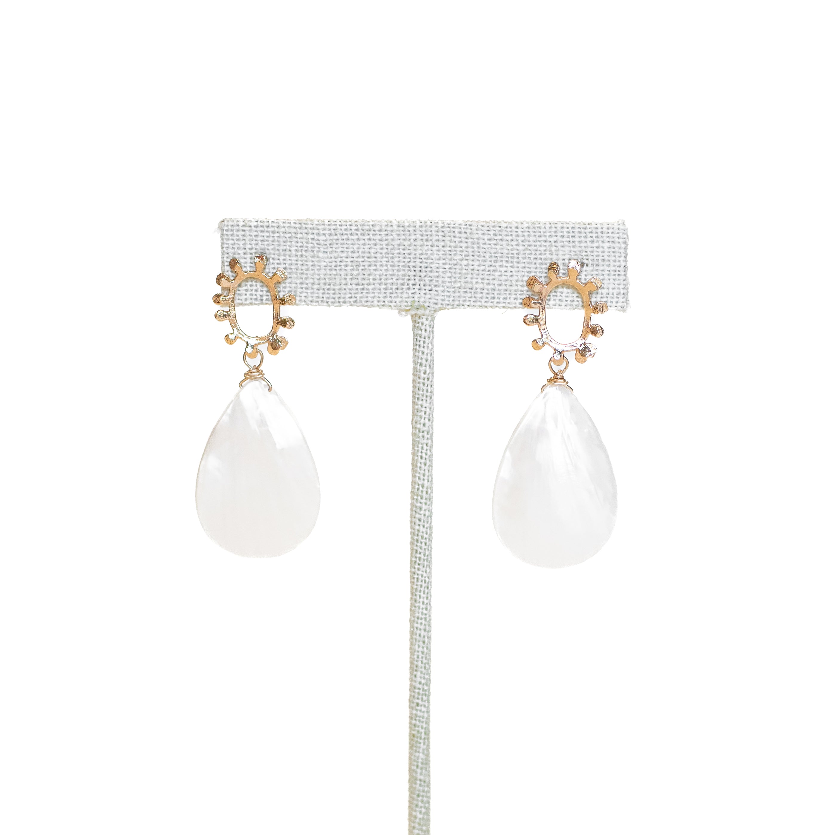Large mother of pearl tear drops on a dotted, open-circle, gold-plated stud. Shown on a stand