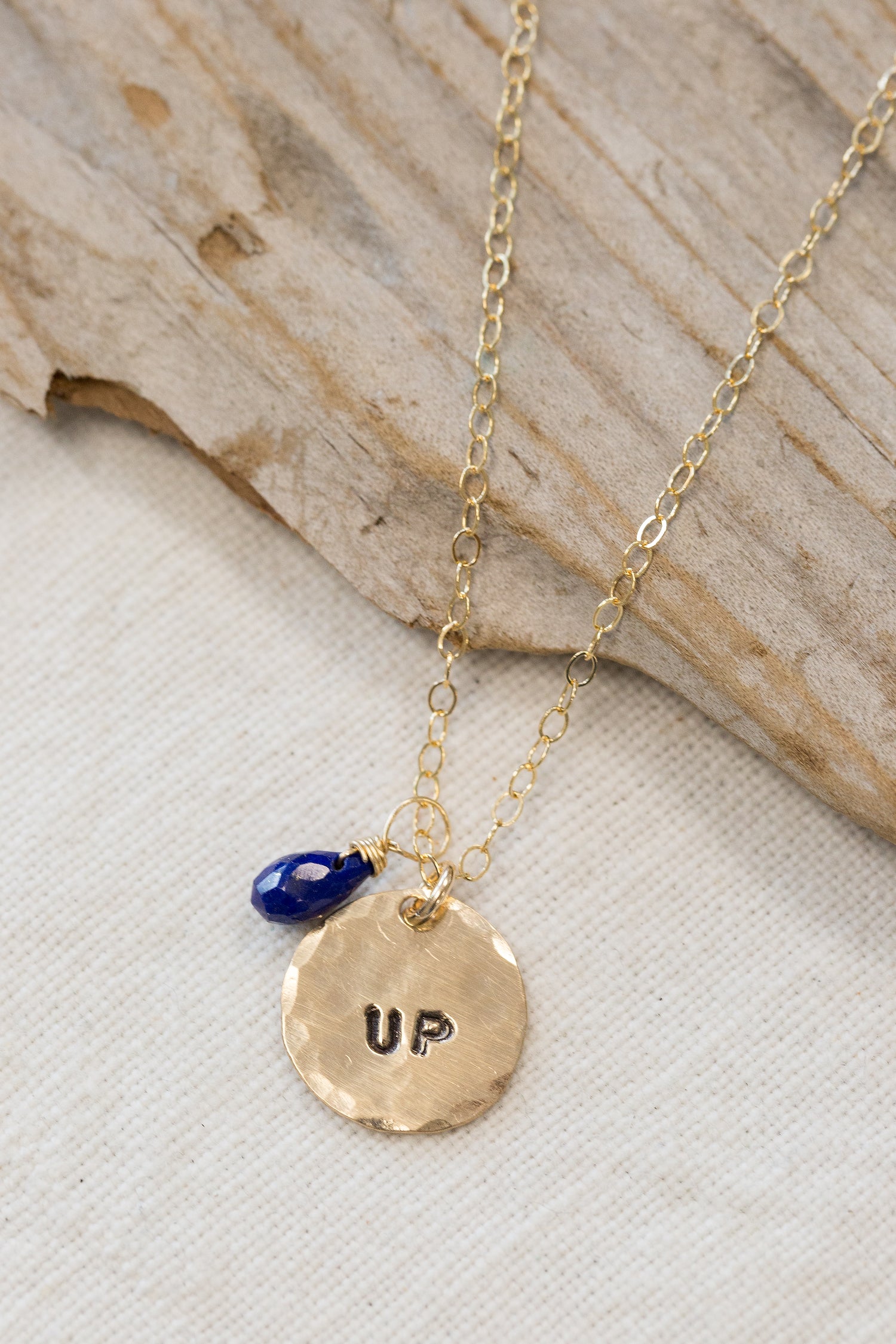 gold filled medium size circle (less than a dime) with the word "up" stamped on it and a blue bead on a gold chain