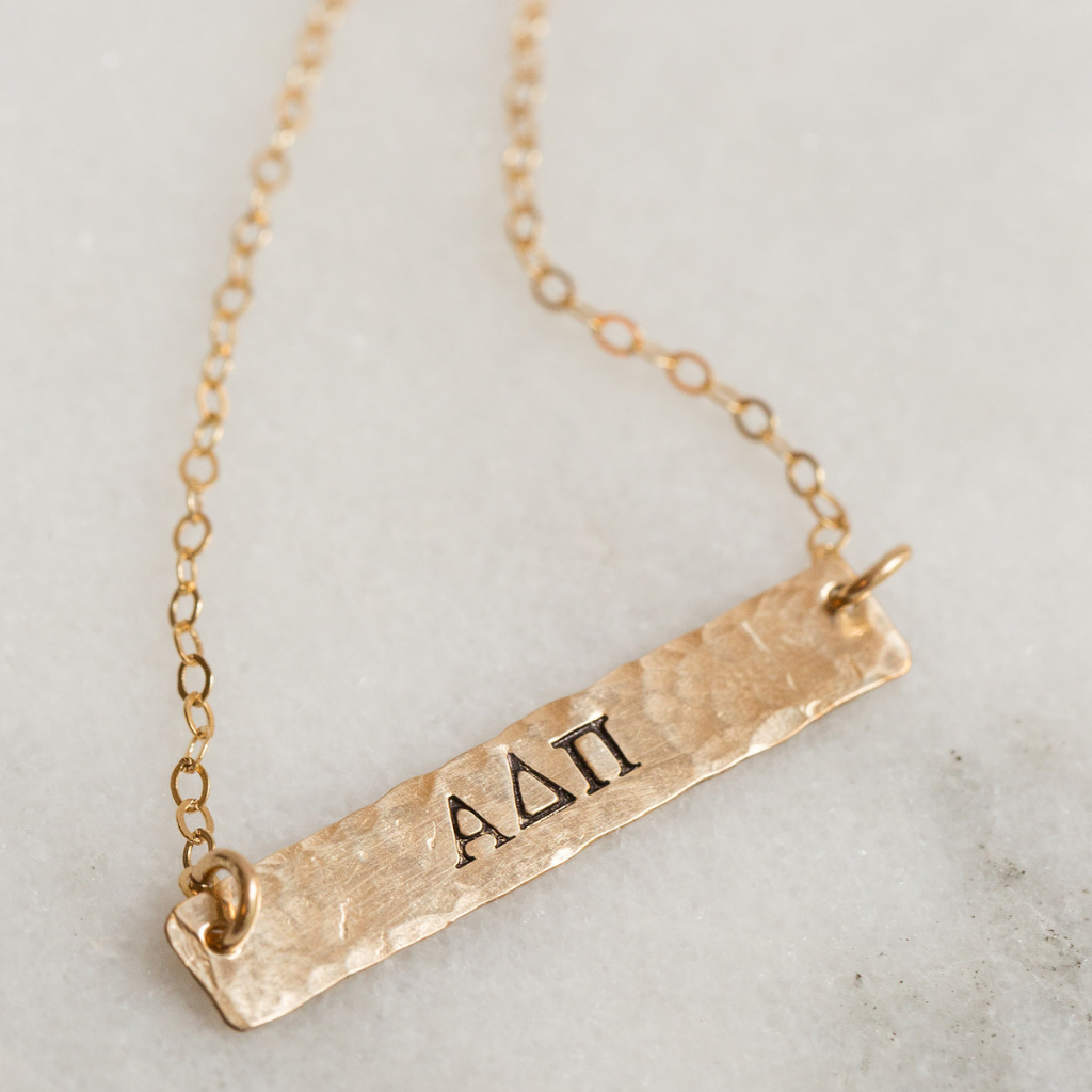 Hand stamped horizontal gold filled bar with phrases on it. Attached to a gold chain.