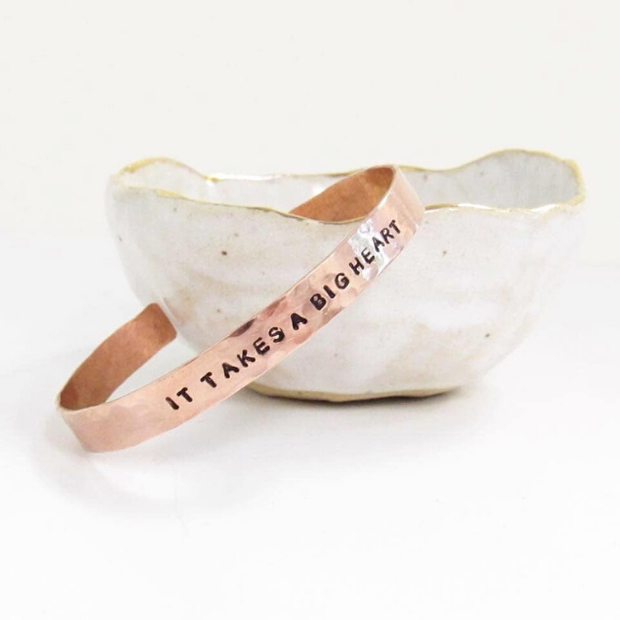 The phrase "It takes a big heart" stamped on the outside of one of our copper cuffs. Displayed in a bowl. 