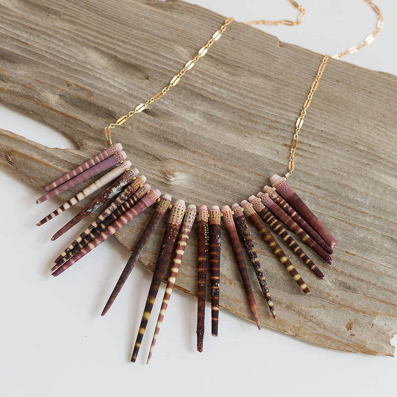 Sea urchin spine necklace attached to gold chain shown on a piece of wood. 